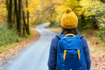 An autumn-dressed hiking woman strolls along a forest road while wearing a knitted sweater, hat, and backpack