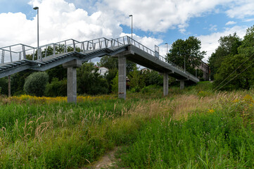 A modern pedestrian bridge spans lush greenery in an urban setting on a sunny day