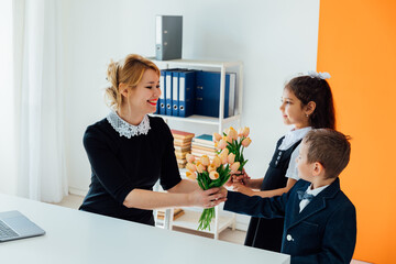 A boy and a girl give flowers to a teacher for a holiday