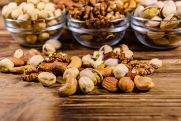 Various nuts (almond, cashew, hazelnut, pistachio, walnut) in glass bowls on a wooden table. Vegetarian meal. Healthy eating concept