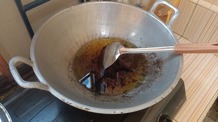 A silver wok with hot oil and a spatula on a stovetop.