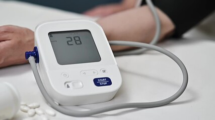 Close-up of a digital blood pressure monitor wrapped around a patient's arm, with medication nearby, highlighting health monitoring and patient care.