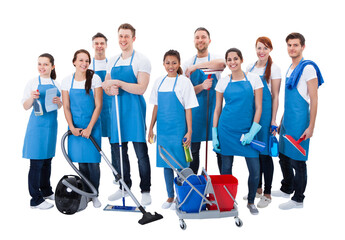 Smiling janitorial team in blue aprons with cleaning equipment isolated