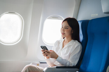 Fototapeta premium Airplane Window View: A young woman with a calm, serene expression, lost in the digital world, gazes out the window of an airplane, capturing the essence of travel, relaxation and the anticipation o