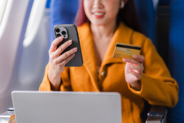 In-Flight Purchases: Asian woman enjoys seamless online shopping experience on airplane, holding credit card and using smartphone. 