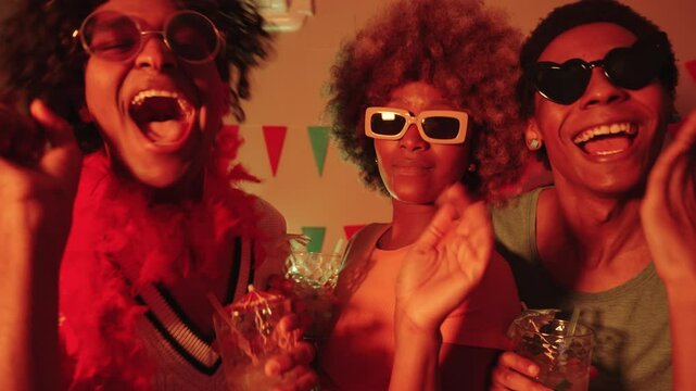 Three LGBTQIA friends, Latino gay couple and Black woman, enjoying mojitos and dancing under colorful lights