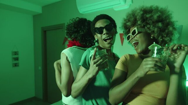 LGBTQIA group, Latino gay couple and Black woman, dancing with mojitos and colorful lights at home