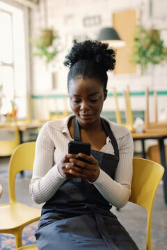 Young black female waitress using mobile phone in cafe