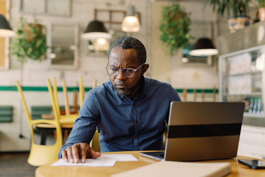 Adult black cafe owner inspecting financial data with laptop