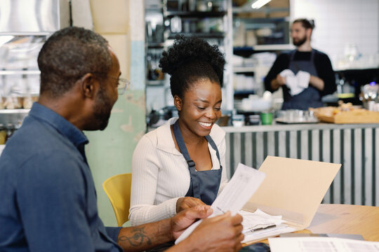 Waitress and cafe owner checking payments near blurred cashier