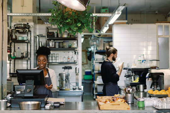 Female cashier or waiter using cash register near waiter in cafe