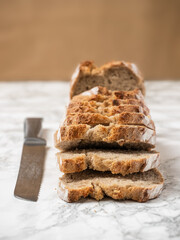 Sourdough sliced bread with a silver knife on the side. Marble counter with a brown background....