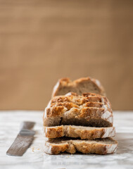 Brown loaf of bread with a silver knife on the side. Marble counter with a brown background. Angle...