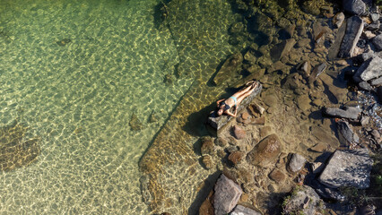 Woman sunbathing on a rock in the middle of crystal-clear waters