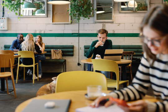 Man using laptop at table near other blurred visitors in cafe