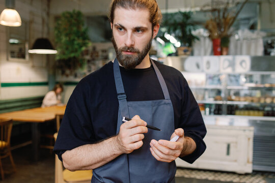 Focused bearded waiter listening order from unknown person in cafe