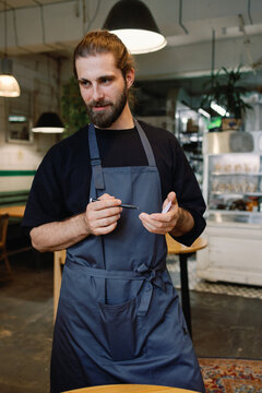 Young male bearded waiter listening order from unknown person in cafe