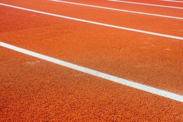 A close-up view of an orange running track with white lane markings, emphasizing the precision and order of athletics.