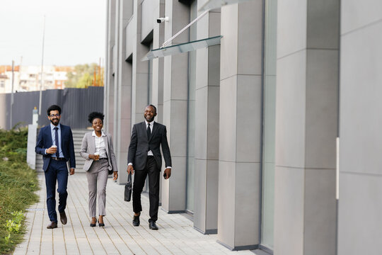 Joyful businesspeople strolling past facade of office building