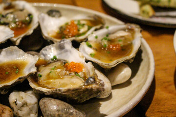 Fresh oysters sit on top of rocks, garnished with roe, soy sauce, and fresh chives, ready to be slurpled.