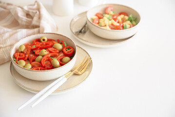 Healthy vegetarian salad with fresh cherry tomato, cucumber, sweet pepper, green olives and lettuce in bowl on white table