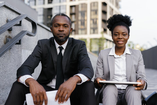 Corporate manager and his assistant sitting on staircase outdoors 