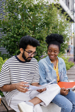 Concentrated teacher checking homework of smiling student in park