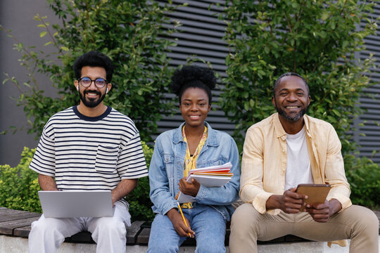 Coworkers and manager seated on bench outdoors smiling at camera