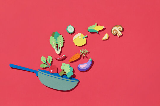 Fresh vegetables falling into a pan on the red background