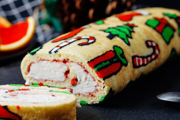 Biscuit Christmas roll dessert with traditional Christmas colorful patterns and cream cheese on black board. Close up, Side view.