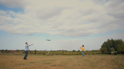 Happy Caucasian family father male man dad little boy son child kid schoolboy playing game throwing launching toy airplane plane enjoy activities together nature field meadow. Weekend trip fatherhood