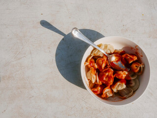 Small bowl with russian style dumplings covered with ketchup and dill on a light color table. Tasty portion of food for a lunch. Cooked simple meal served for one person.