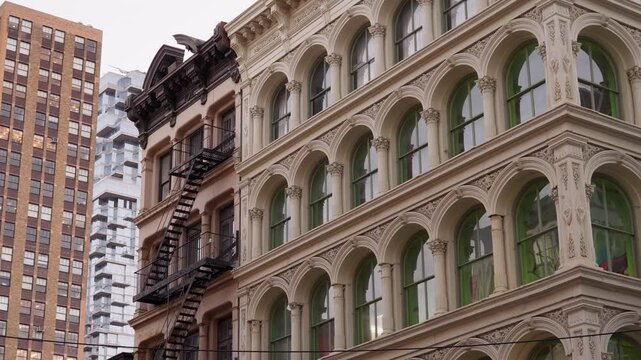 A close-up of contrasting architectural styles in Soho, NYC, showcasing historic iron fire escapes alongside modern glass and brick structures.