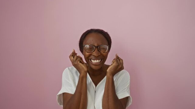Luck smiling, young african american woman wearing glasses, fingers crossed, eyes closed in hope, gesturing over isolated pink background, superstitious and standing happy
