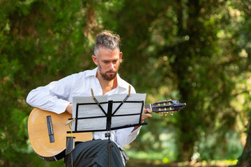 Musician playing acoustic guitar reading music score in a forest
