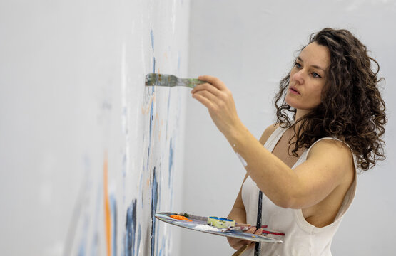 Focused sexy beautiful pretty mature artist woman female painter meticulously paints on a large canvas, her creative energy flowing with each brushstroke