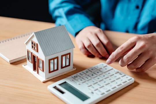 residential, financial, rental, finance, investment, agreement, asset, estate, insurance, calculate. A person is using a calculator to calculate. The house is a small white model on a table.