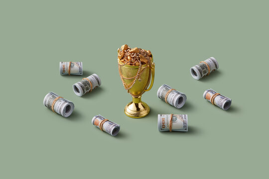 Bundles of dollar bills laying around golden cup with jewels