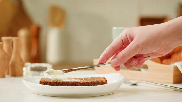 Cream cheese Spreading with knife on toasted bread slice, women hands apply fresh butter cream cheese on a slice of freshly baked bread close up, morning breakfast.