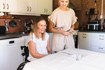 Woman with a Disability Enjoying Lunch with Assistant in Kitchen