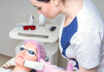 Young woman receiving laser treatment in cosmetology clinic. Eyes covered with protection glasses