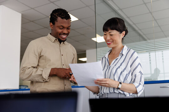 Happy colleagues discussing over document in office