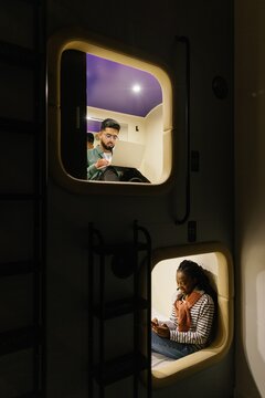 Male student typing laptop while woman using smartphone in mini-rooms
