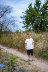 Young child walking along a dirt path surrounded by wildflowers. A young boy in a white shirt stands on a dirt path, smiling amidst tall grass