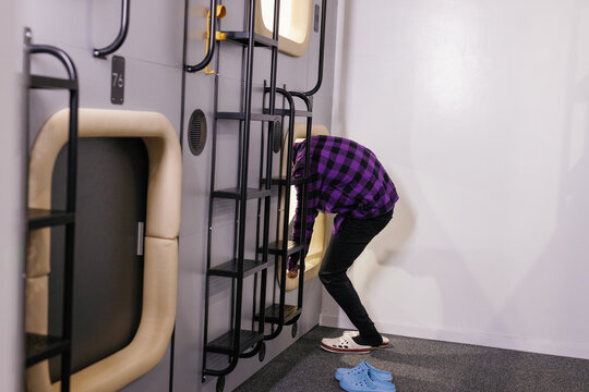 Partial man entering to tiny mini-room of economy-class capsule hotel
