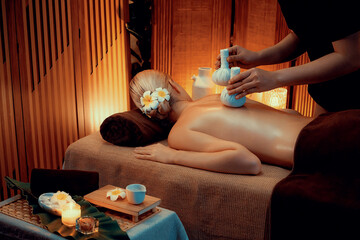 Hot herbal ball spa massage body treatment, masseur gently compresses herb bag on woman body....