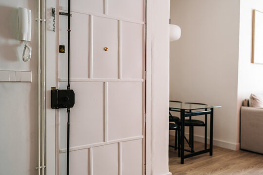 A white wooden door secured with multiple locks stands slightly ajar