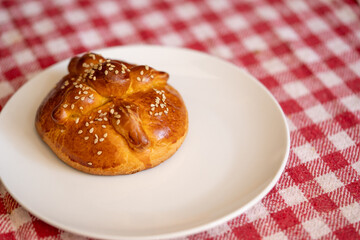 Plato blanco con un pan de muerto con ajonjolí sobre mantel a cuadros rojos
