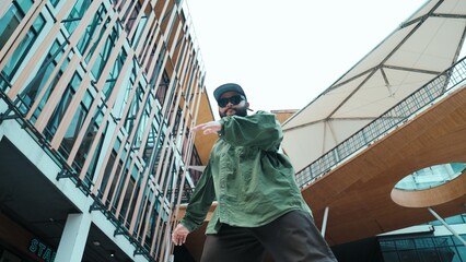 Low angle view of hipster pose in hip hop style surrounded by mall view. Portrait of sporty asian hip hop choreographer dancing break dance while looking at camera. Outdoor sport 2024. Hiphop.
