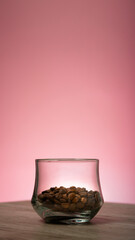 Closeup of roasted coffee beans in a glass on pink background